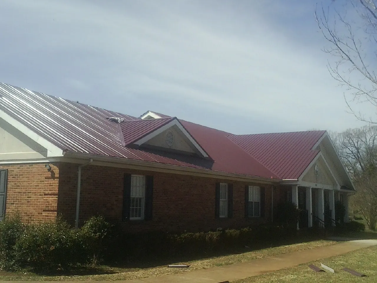 Red metal roof with gabled entries on a long brick building, from a Hail Damage Roof Repair job in Falls Village
