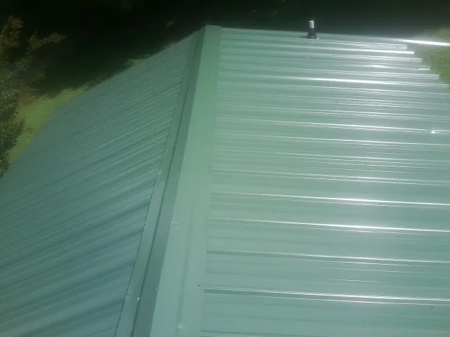 New green metal panels meeting at the ridge of a roof — Flat Roof Repair work by our crew in Falls Village