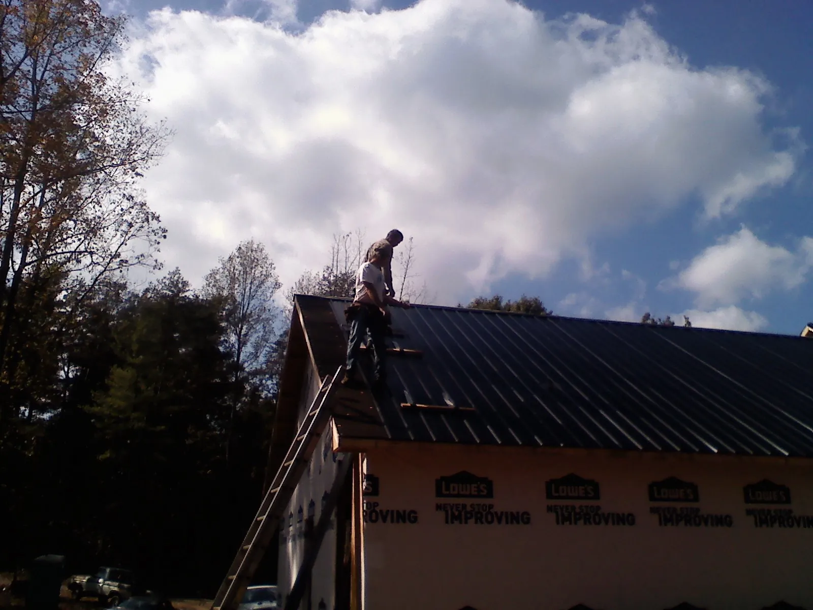 Roofer fastening dark metal panels high against a cloudy sky, from a Roof Inspection job in Falls Village