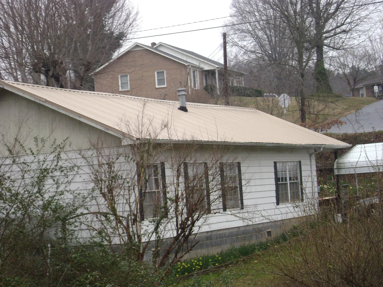Tan metal roof on a white sided house set into a hillside — Commercial Roofing by Roofing Brothers in Falls Village
